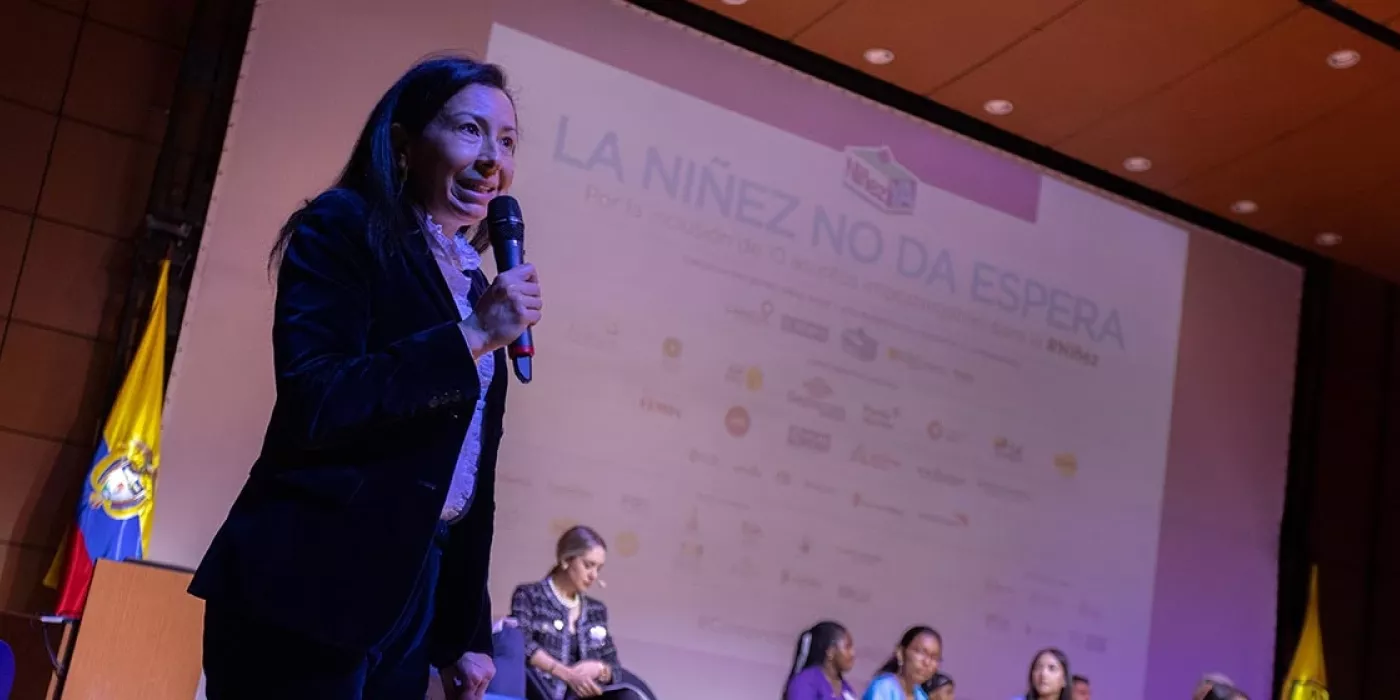 Mujer hablando por micrófono en un escenario.