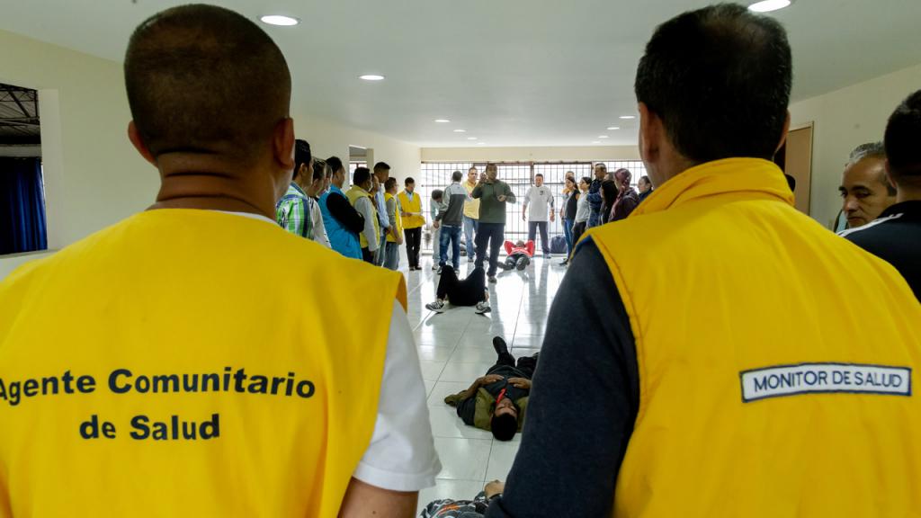 Dos hombres visten chaleco amarillo en el que se lee:  Agente comunitario en salud.
