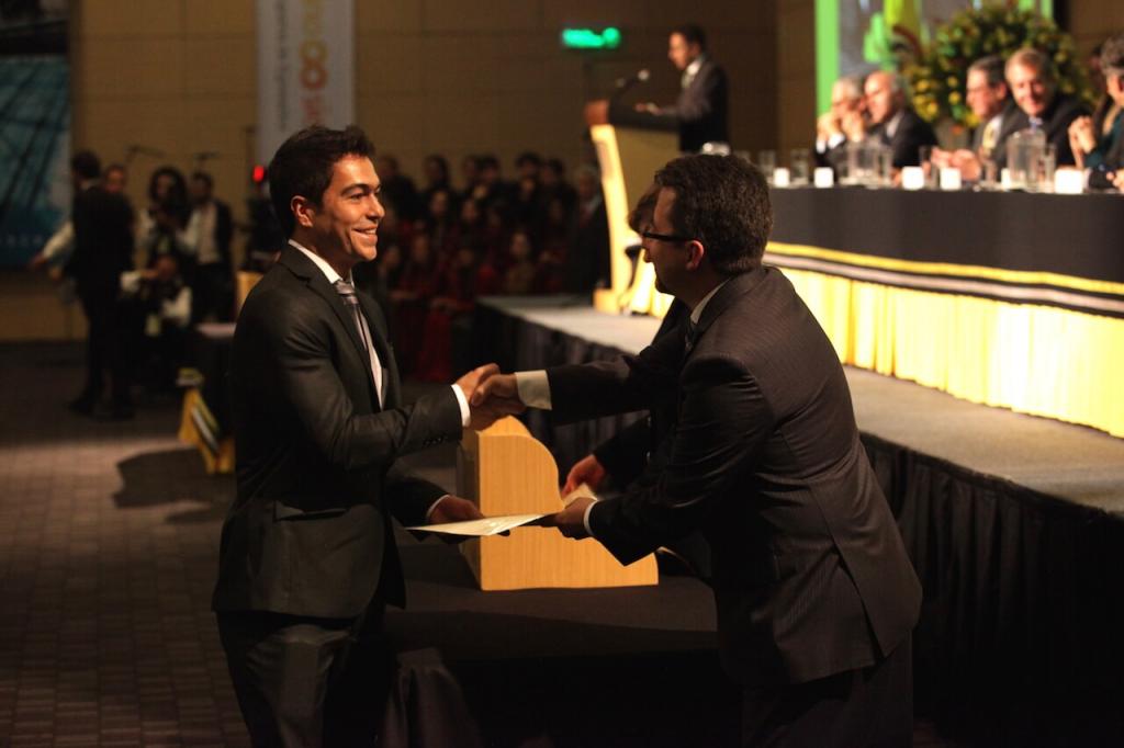 un joven de traje negro da la mano a un hombre que le entrega diploma