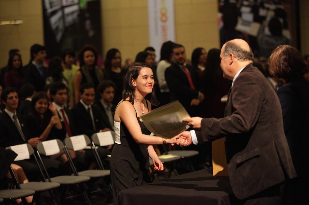 una joven con vestido blanco y negro recibe diploma de grado