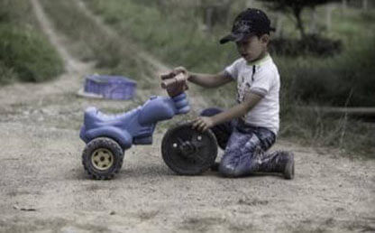 Niño juega con un triciclo roto en una carretera rural