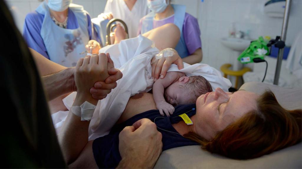 Mujer en un parto, cargando a su bebé.