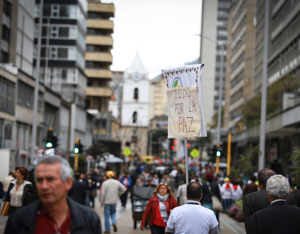 Peatones en las calles del centro de Bogotá. Una de ellas levanta un pequeño cartel que dice: 'Todo por la paz'.