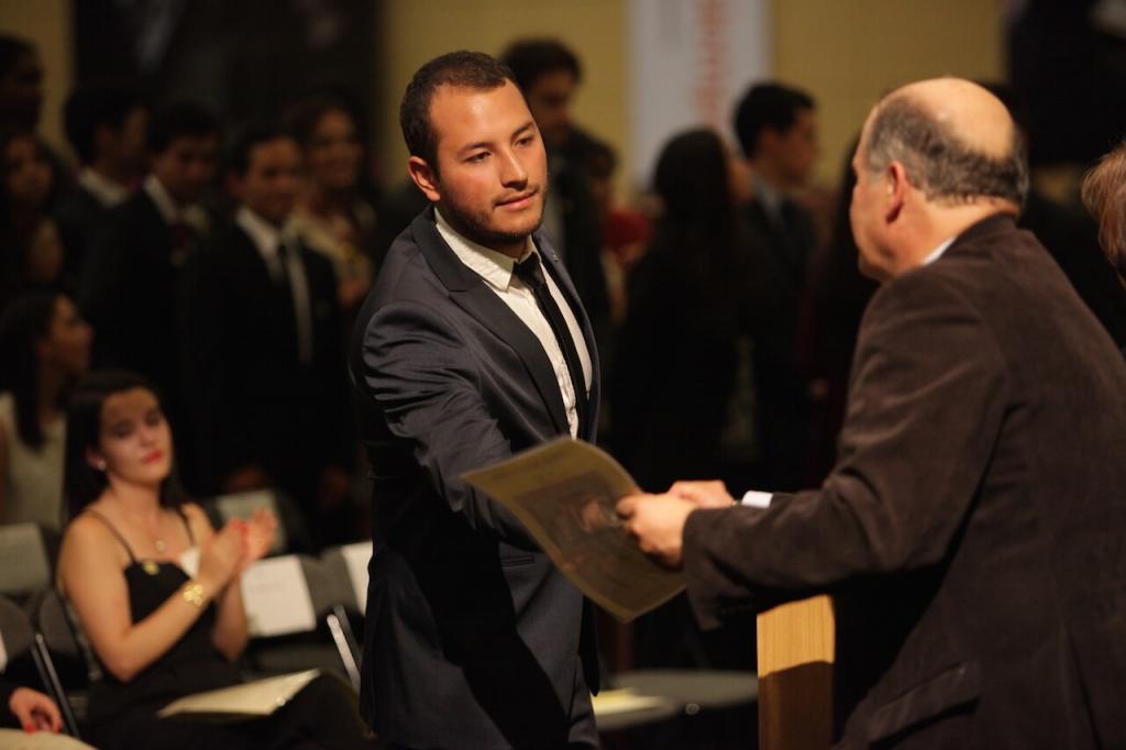 joven de traje gris y corbata negra recibe diploma de grado
