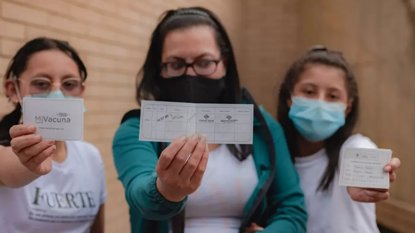 Mamá con sus dos hijas mostrando el carné de vacunación