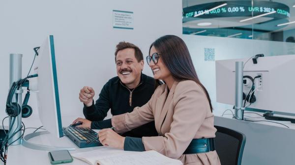 Una mujer con gafas y un hombre sonrientes revisando información en un monitor de computadora durante una sesión de estudio sobre posgrados Maestrias, especializaciones y doctorados