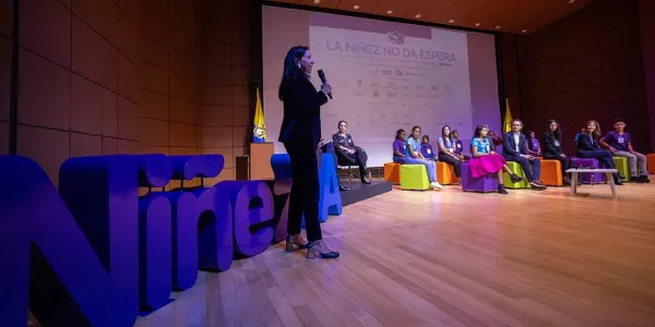 Mujer hablando por micrófono en un escenario.