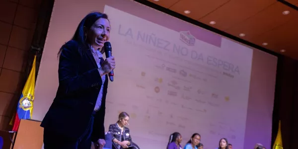 Mujer hablando por micrófono en un escenario.