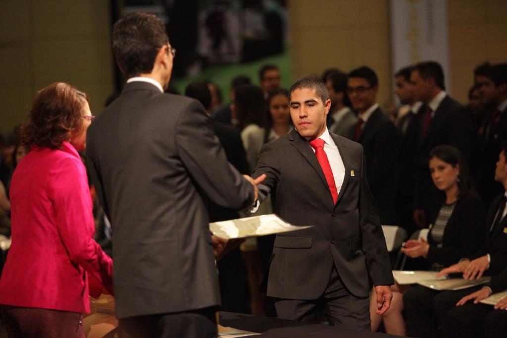hombre de traje negro y corbata roja recibe diploma de dos personas